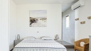 Ein Schlafzimmer mit einem Bett, zwei Nachttischen, einem Sessel und einer Wand-Klimaanlage.