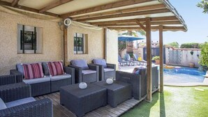 Eine Außenpatio-Terrasse mit Korbmöbeln, einem Pool und einem überdachten Bereich.