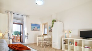 En stue med sofa, fjernsyn, bogreol og et spiseområde med bord og stole.
