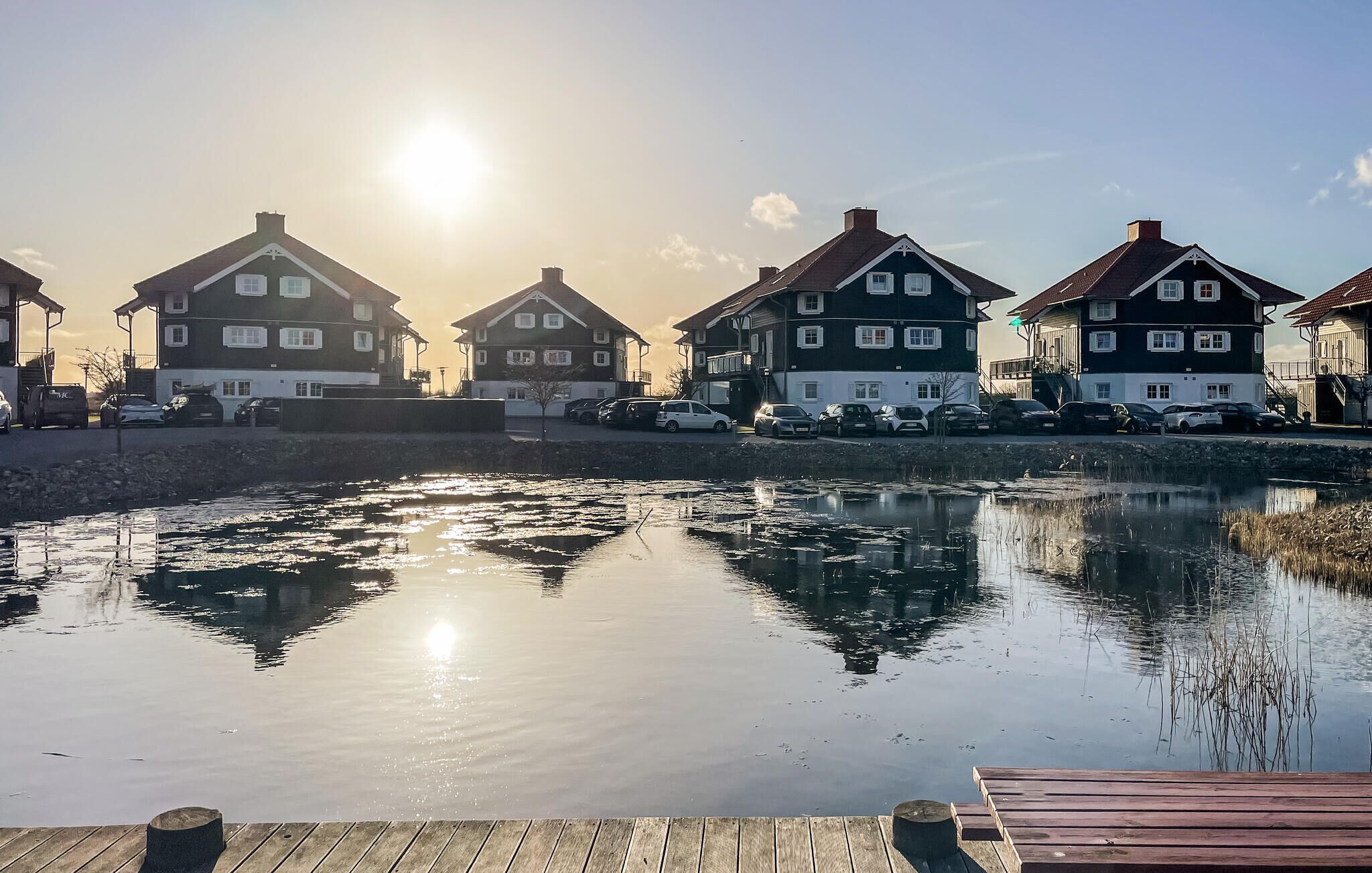 Række af huse ved et roligt vandareal med en træbro i forgrunden.