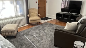 Een woonkamer met een leren bank, een grijze vloerkleed, een houten vloer, een televisie en een deur met een raam.