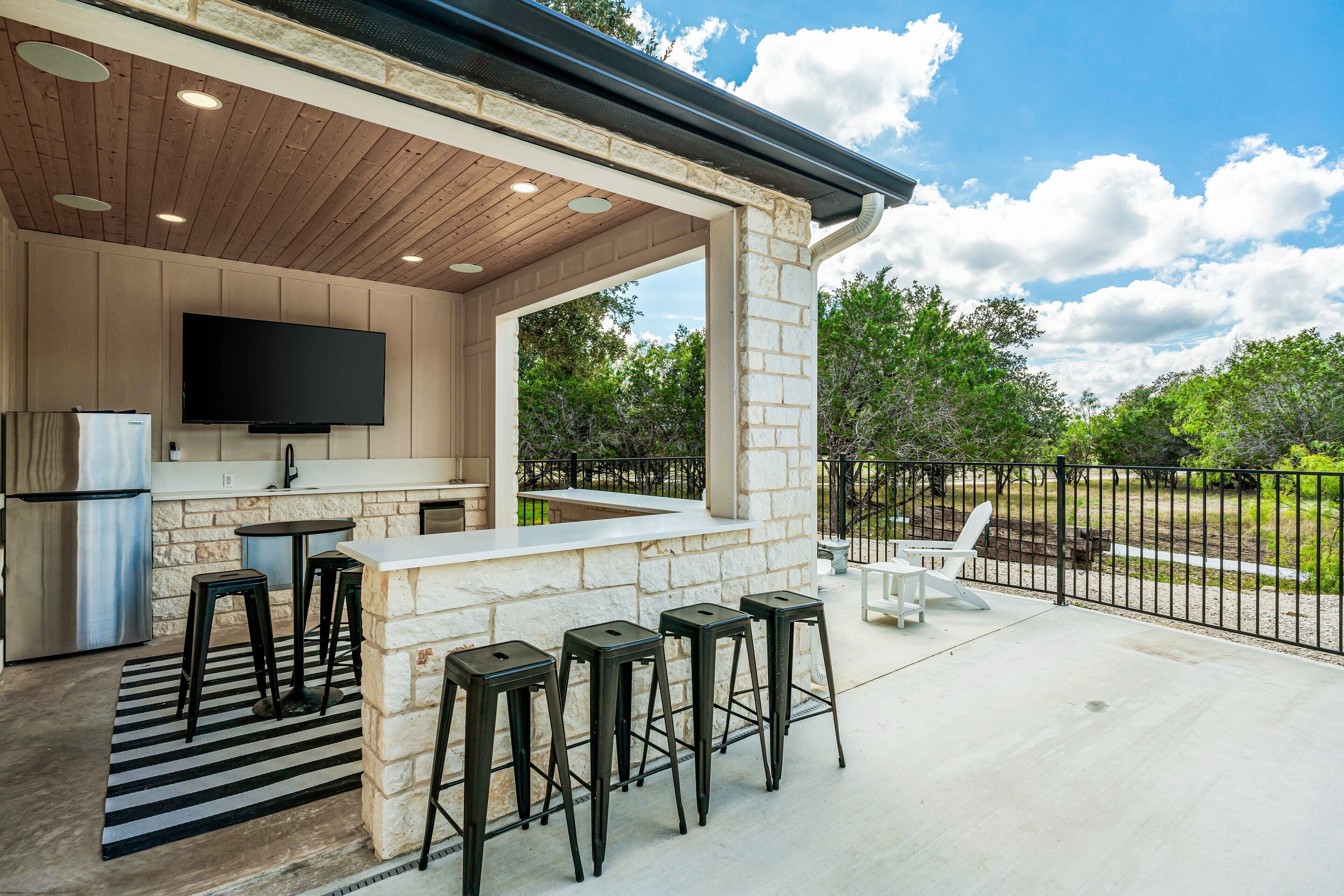 An outdoor kitchen with a stone wall, a flat-screen TV, and bar stools.