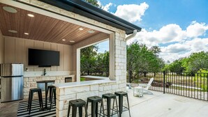 An outdoor kitchen with a stone wall, a flat-screen TV, and bar stools. - Hot tub, pool, Sonos speaker system (Concan)