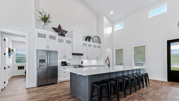 A modern kitchen with white cabinets, a large island with bar stools, and a stainless steel refrigerator. - Hot tub, pool, Sonos speaker system (Concan)