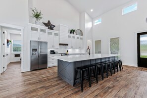 A modern kitchen with white cabinets, a large island with bar stools, and a stainless steel refrigerator.