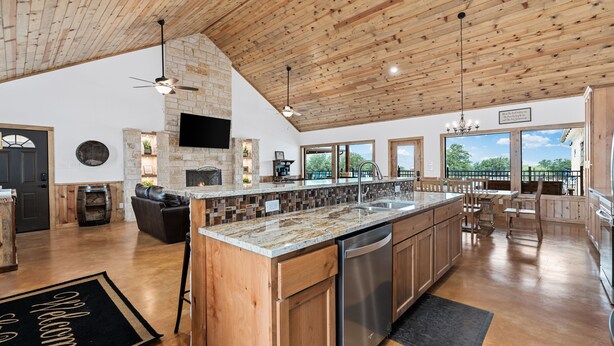A spacious kitchen with wooden cabinets, a large island, and a stone fireplace. - Outdoor kitchen, volleyball, swimming pool & hot tub! (Concan)