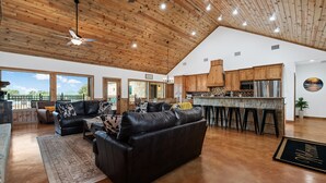 A spacious living area with a large leather sofa, wooden ceiling, and a kitchen with a bar. - Outdoor kitchen, volleyball, swimming pool & hot tub! (Concan)