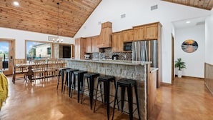A spacious kitchen with wooden cabinets, a stainless steel refrigerator, and a bar area with stools. - Outdoor kitchen, volleyball, swimming pool & hot tub! (Concan)