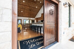 A wooden door with a welcome mat, a stone wall, and a bar area with stools.