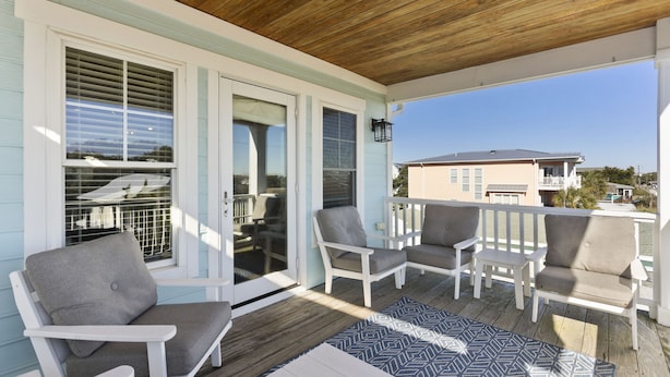 A covered porch with white chairs and a patterned rug.