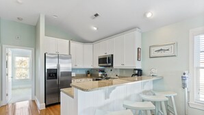 A modern kitchen with white cabinetry, stainless steel appliances, and a central island with bar stools.
