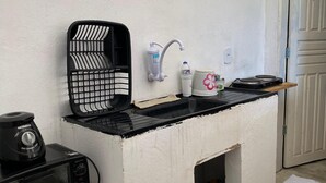 Uma cozinha compacta com bancada preta, um purificador de água, chaleira e uma pia pequena.