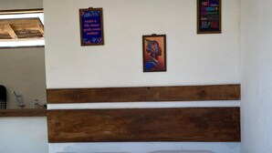 Uma cama com roupa branca e cabeceira de madeira, dois travesseiros e um cobertor. Há duas decorações na parede, uma com texto e outra com uma imagem colorida.