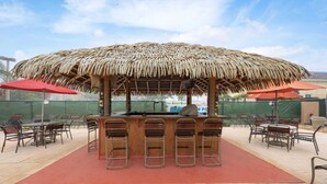 An outdoor bar area with a thatched roof, multiple bar stools, and red umbrellas. - Cozy Stylish Townhome (Davenport)