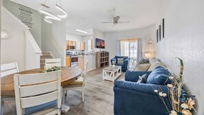 A modern living room with a blue sofa, a wooden dining table, and a kitchen in the background. - Cozy Stylish Townhome (Davenport)