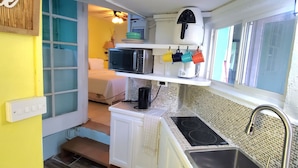 Une cuisine compacte équipée d’un évier, d’une cuisinière et d’un four à micro-ondes. Une petite marche mène à l’espace chambre.