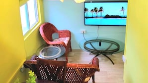 Un espace de vie compact comprenant un ventilateur de plafond, un téléviseur diffusant une scène de plage, une table à manger avec des chaises et une petite table ronde.