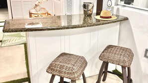 A kitchen with a central island, two wicker stools, a ceiling fan, and a window with blinds. - MIAMI LUX HOUSE / Pool / Lounge / Bar (Miami)