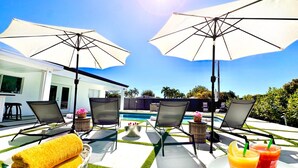 A poolside area with lounge chairs, umbrellas, a pool, and a table with drinks and towels. - MIAMI LUX HOUSE / Pool / Lounge / Bar (Miami)