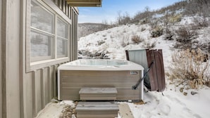 Un jacuzzi en el exterior de una casa, con escalones que llevan a él, rodeado de nieve y un paisaje montañoso.