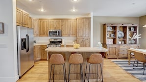 Una cocina moderna con armarios de madera, electrodomésticos de acero inoxidable y una isla central con taburetes de bar.