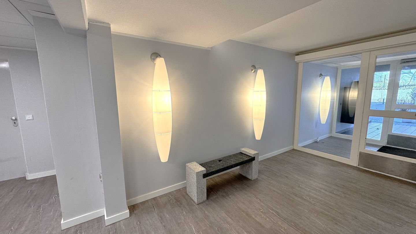 A modern interior with a bench, two wall-mounted lights, and a view through a glass door.