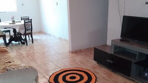 A living room with a wooden floor, a TV stand, and a dining area with a table and chairs. - Recanto Silvia Timbó (Tapera)
