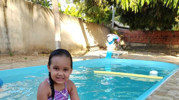 A child sitting by a swimming pool with a mermaid tail. - Recanto Silvia Timbó (Tapera)
