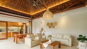 A spacious living area with a high ceiling, wicker furniture, and a dining set.