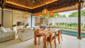 A spacious outdoor area with a wooden dining table, wicker furniture, and a pool.
