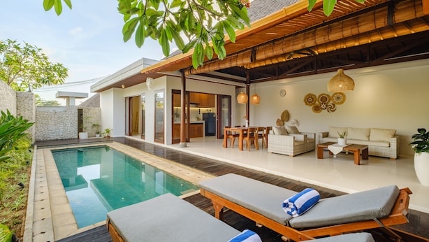 A modern outdoor pool area with lounge chairs, a dining area, and a living space with a sofa and coffee table.
