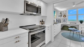 A modern kitchen with white cabinetry, a built-in oven, a microwave, and a dining area with a view of the sea. - Enjoy this beautiful condo at St. Maarten in gorgeous, coastal Pelican Bay! (Naples)