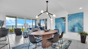 A modern dining area with a round wooden table, black chairs, and a blue abstract painting on the wall. - Enjoy this beautiful condo at St. Maarten in gorgeous, coastal Pelican Bay! (Naples)
