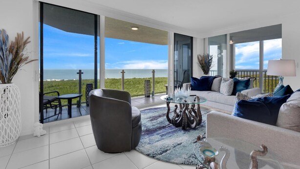 A spacious living room with a large glass door leading to a balcony with a view of the sea. - Enjoy this beautiful condo at St. Maarten in gorgeous, coastal Pelican Bay! (Naples)