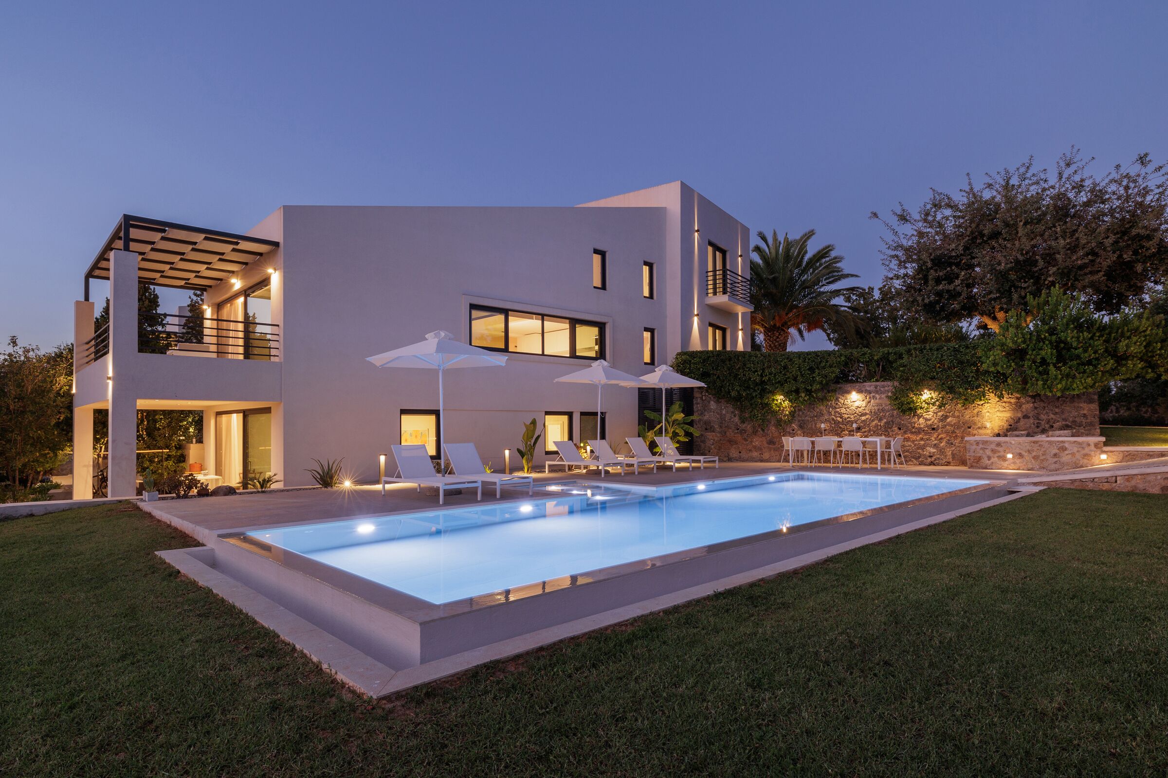 Een modern huis met twee verdiepingen, een zwembad, buitenzitplaatsen en een goed verlicht terras.