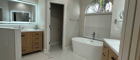 A modern bathroom with a freestanding bathtub, a large mirror, and wooden cabinetry.