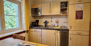 A kitchen with wooden cabinets, a stainless steel dishwasher, a microwave, and a window with a view of greenery.