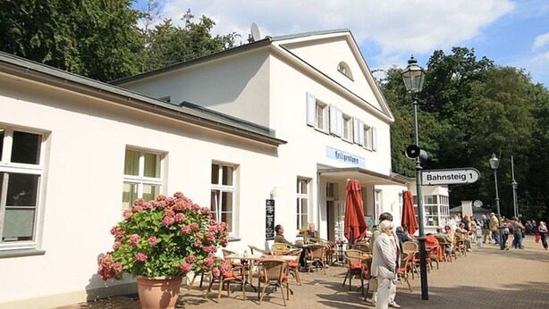Ein Gebäude mit Außenbestuhlung und einem Schild, das "Bahnsteig 1" anzeigt.
