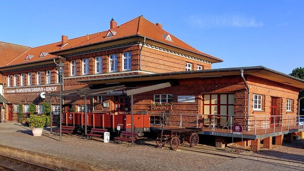 A historic train station with a brick building, a covered waiting area, and a vintage cart. - Mollibahnhof West - Ferienwohnung 01 - Mollibahnhof - Kühlungsborn West (Kühlungsborn)