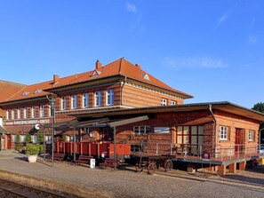 En historisk tågstation med en byggnad i tegel, ett överbyggt väntområde och en gammal vagn.