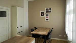 A dining area with a wooden table and four chairs, a white cabinet, and a beige wall with three framed pictures. - Mollibahnhof West - Ferienwohnung 01 - Mollibahnhof - Kühlungsborn West (Kühlungsborn)