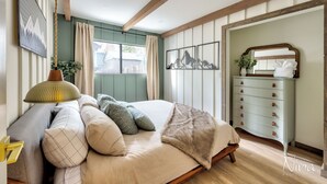 Un dormitorio con cama, cómoda, espejo y obras de arte en las paredes.