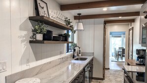 Una cocina moderna con dos fregaderos, encimeras de mármol, vigas de madera y vistas al comedor.