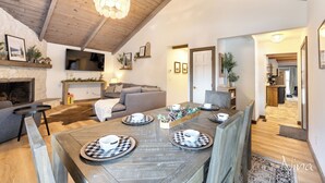Una sala de estar acogedora con chimenea, una mesa de comedor preparada para cuatro personas y una cocina al fondo.