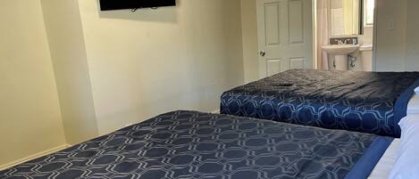 A hotel room with two beds, a television mounted on the wall, and a bathroom visible through an open door.