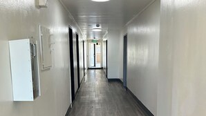 A long, narrow hallway with a wooden floor and white walls. There are doors on both sides and a light fixture on the ceiling. - Budget Inn Hollywood (Los Angeles)