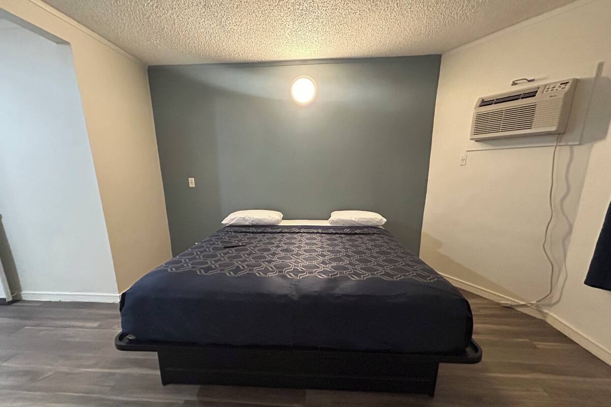 A bedroom with a bed, a wall-mounted air conditioner, and a door.