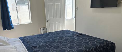 Een slaapkamer met een bed, een televisie aan de muur en een raam met gordijnen.