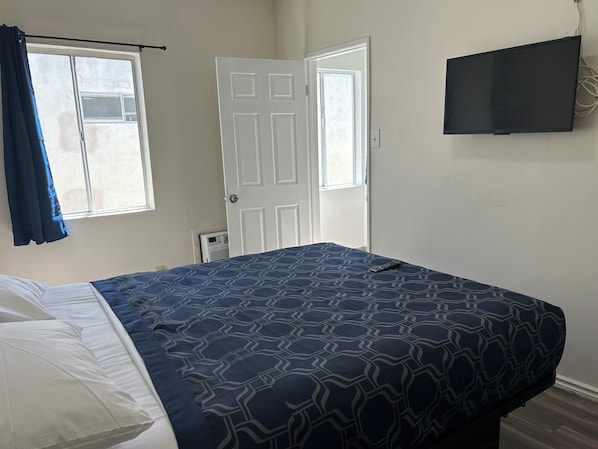 Un dormitorio con cama, televisor en la pared y ventana con cortinas.