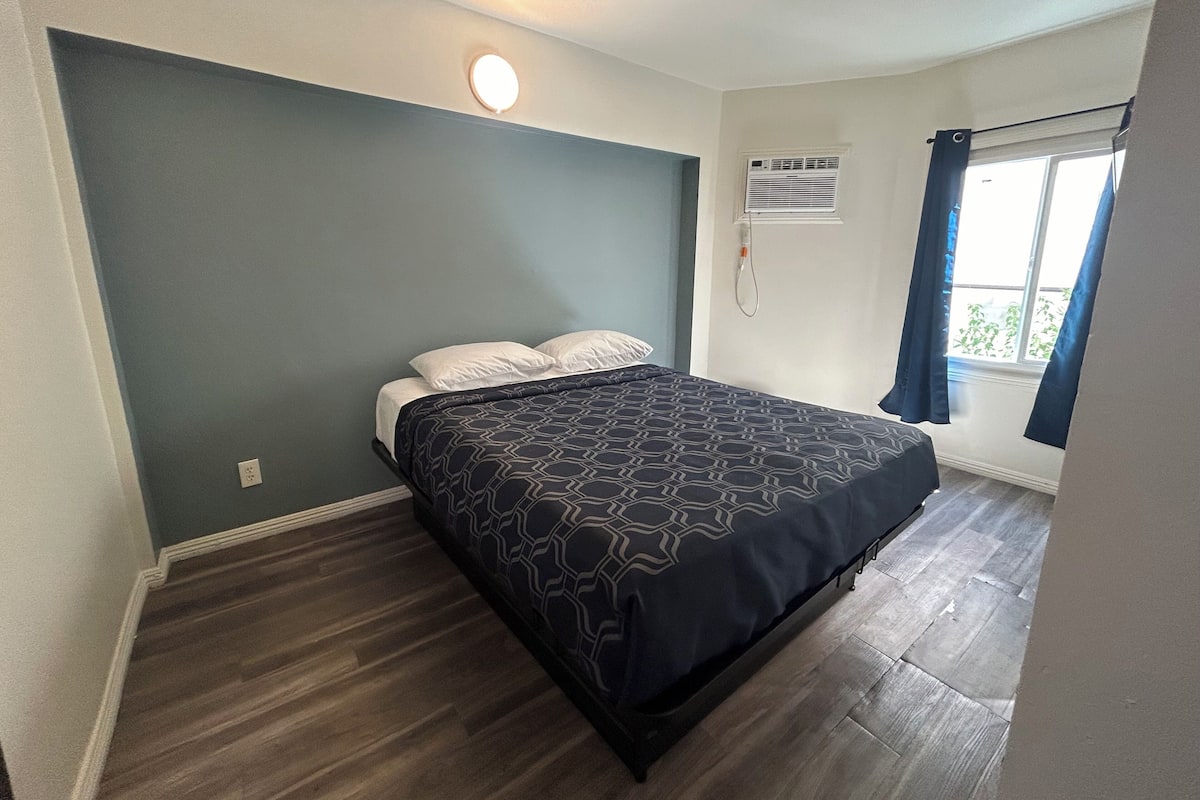 A bedroom with a bed, a wall-mounted air conditioner, and a window with curtains.
